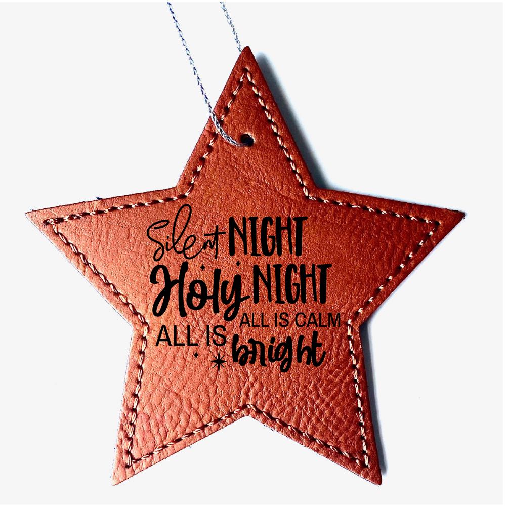 Close up photo of the star-shaped faux leather Chestnut Christmas ornament. The Christmas sain: "Silent Night Holy Night all is calm all is bright" is engraved onto the front side.