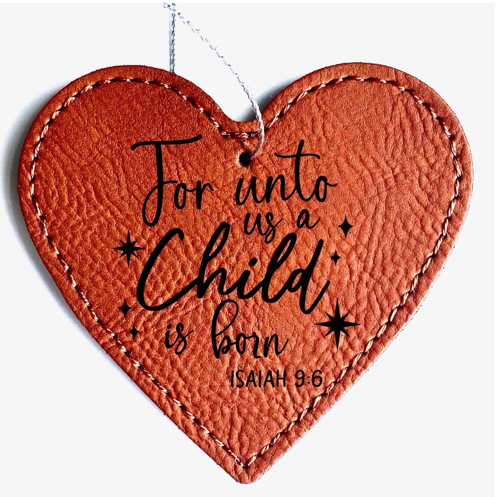 Close up photo of the heart-shaped faux leather Chestnut Christmas ornament. The Bible verse: "For unto us a Child is born Isaiah 9:6" is engraved onto the front side.